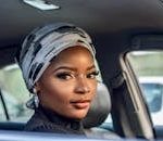 Portrait of a beautiful woman wearing a headscarf sitting inside a car, showcasing elegance and beauty.
